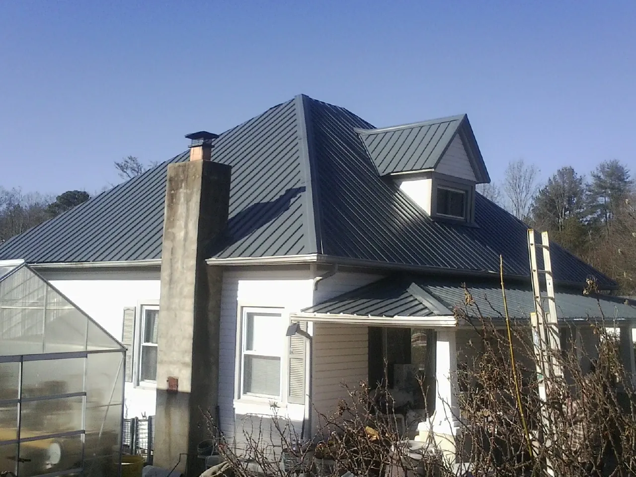 Dark blue standing seam metal roof on a white farmhouse with dormer — Slate & Tile Roof Repair by Roofing Brothers in Driggs