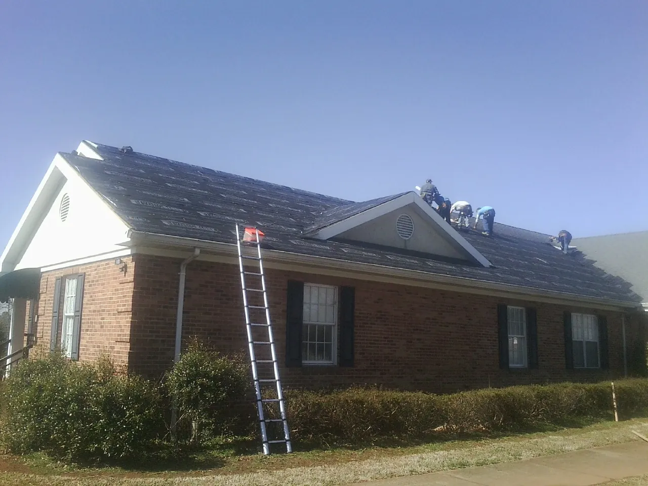Crew tearing shingles off a brick ranch roof with a ladder set — Emergency Roof Repair work by our crew in Driggs
