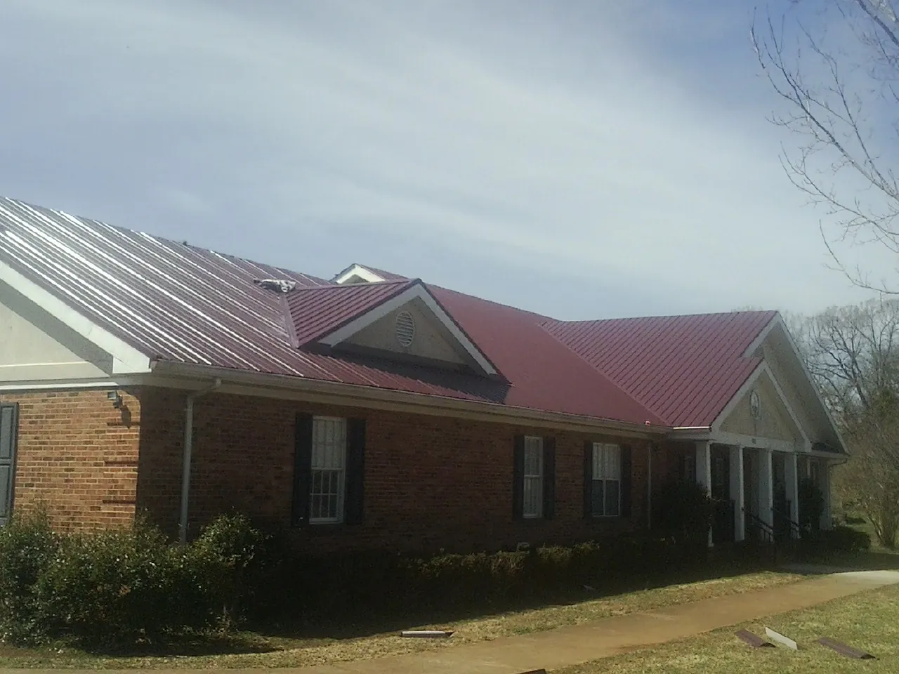 Red metal roof with gabled entries on a long brick building, from a Hail Damage Roof Repair job in Driggs