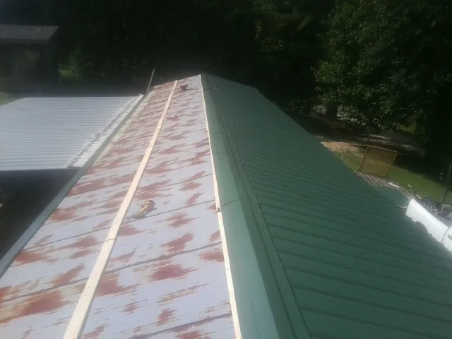 Old rusted panels beside newly installed green metal roofing — Wind Damage Roof Repair by Roofing Brothers in Driggs