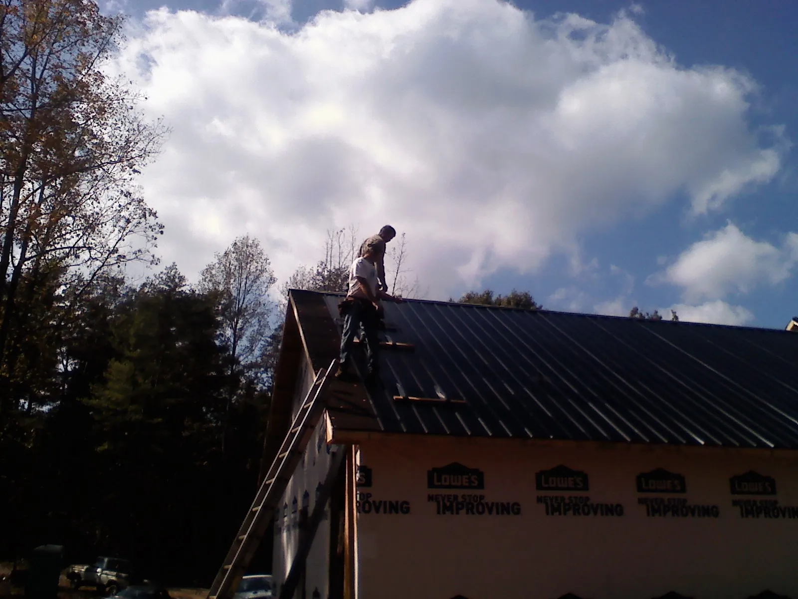 Roofer fastening dark metal panels high against a cloudy sky, from a Roof Inspection job in Driggs