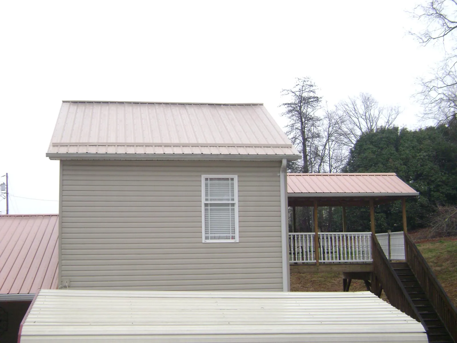 Tan metal roofs on a two story addition and attached porch, from a Roof Replacement job in Driggs